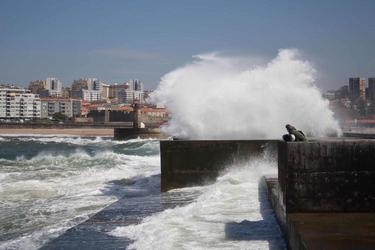 A wave breaking over the sea wall at Foz do Douro with the city behind